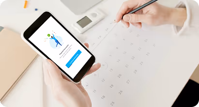 Person holding a smartphone displaying a confirmation screen while marking a date on a calendar with a pencil.