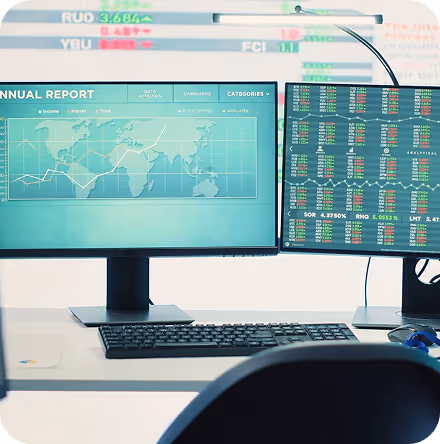 Desk with two computer monitors displaying financial data, stock charts, and an annual report, accompanied by a keyboard and mouse.
