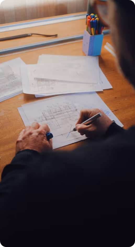 Person sketching architectural plans on paper at a desk with colored pens in a holder.