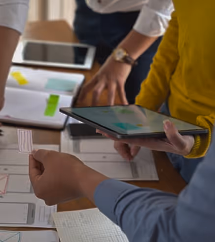 People collaborating at a table with documents and a tablet, reviewing designs or plans.