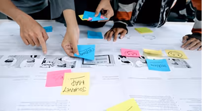 Three people collaborating over a table covered with sketches and colorful sticky notes.