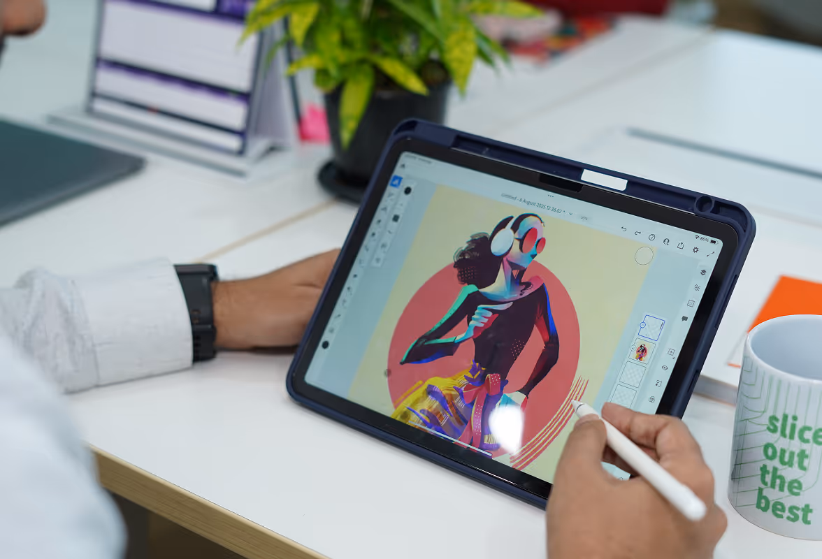 Person using a stylus to create digital art of a colorful abstract figure on a tablet in a workspace.