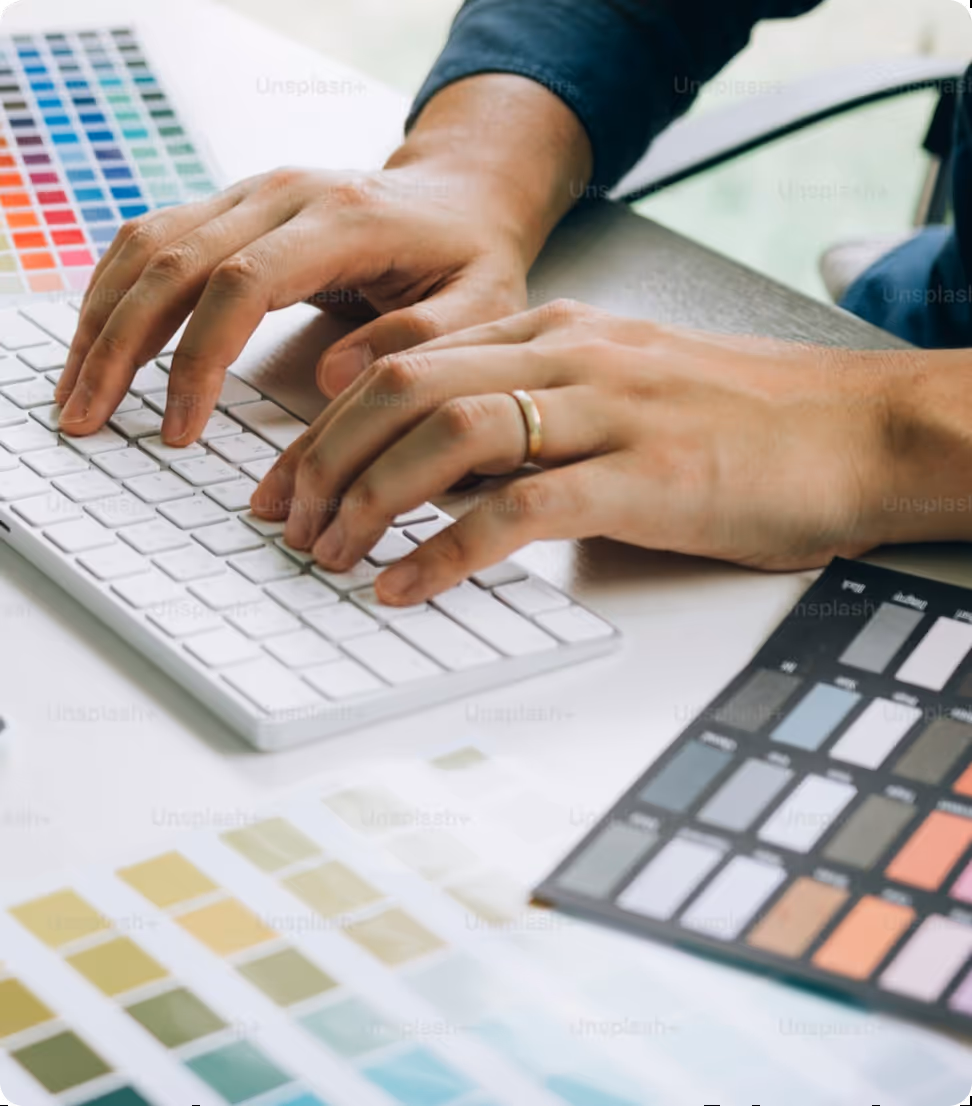 Person typing on a white keyboard surrounded by multiple color swatch samples.