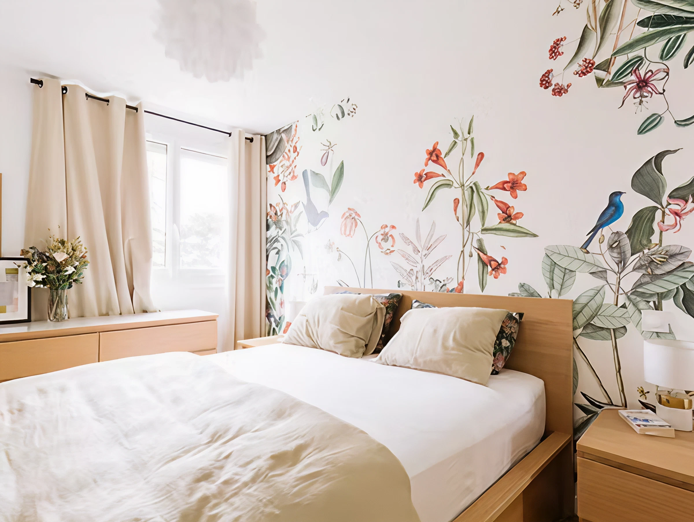 Bright bedroom with wooden bed, floral wallpaper, beige curtains, and bedside table with lamp.