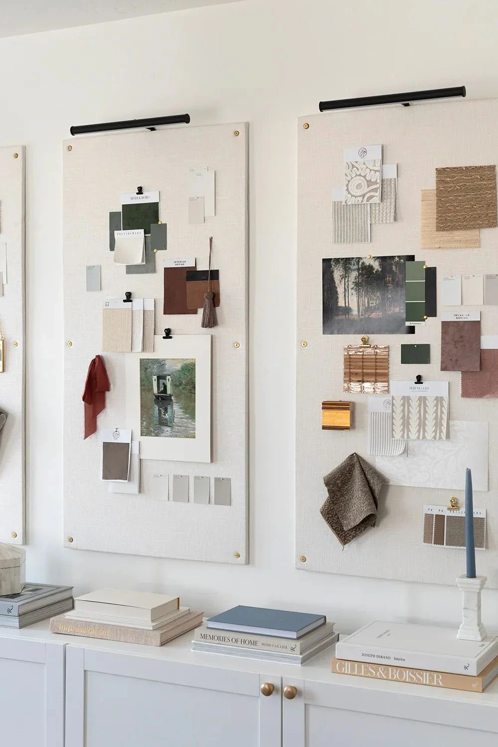 Styled fabric and color sample boards with artwork hanging above white cabinet with books and a blue candle.