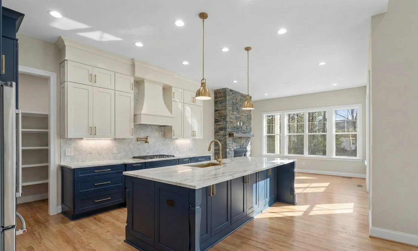 Modern kitchen with beige cabinetry, marble countertops and backsplash, stainless steel appliances, and a central island with a gold faucet.