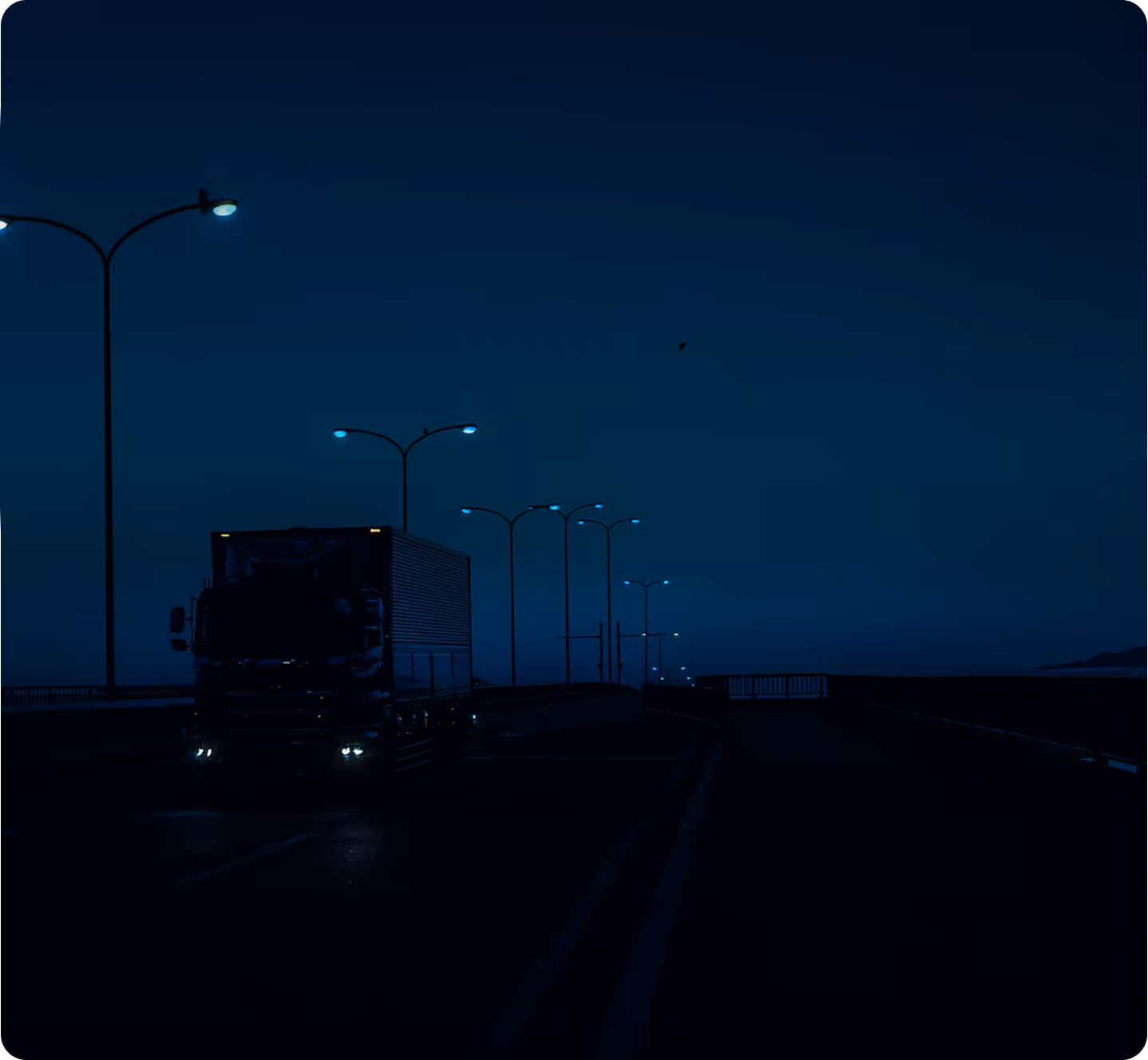 Truck driving on a dimly lit road at night with streetlights glowing blue.