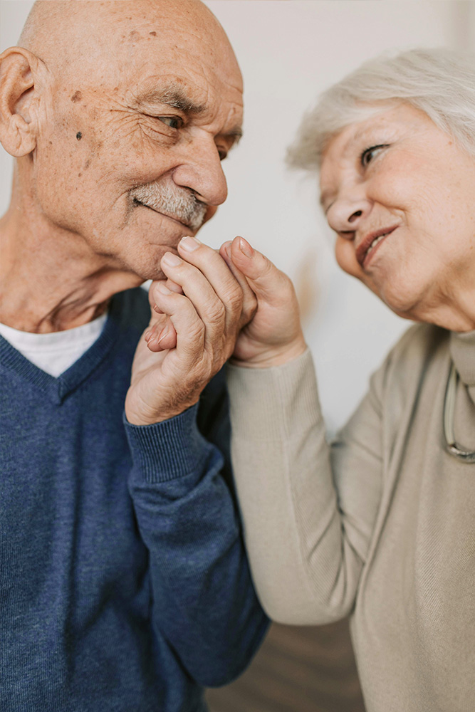 Deux personnes âgées, probablement un couple, se tiennent la main et se regarde.