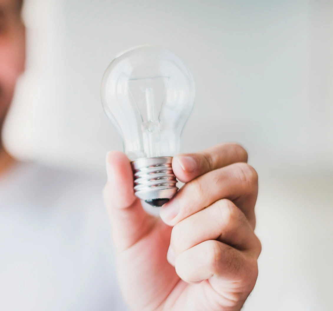 A person holding a clear incandescent light bulb between thumb and fingers against a blurred background.