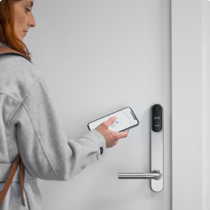 Vrouw gebruikt smartphone om deur te openen met een digitaal deurslot.