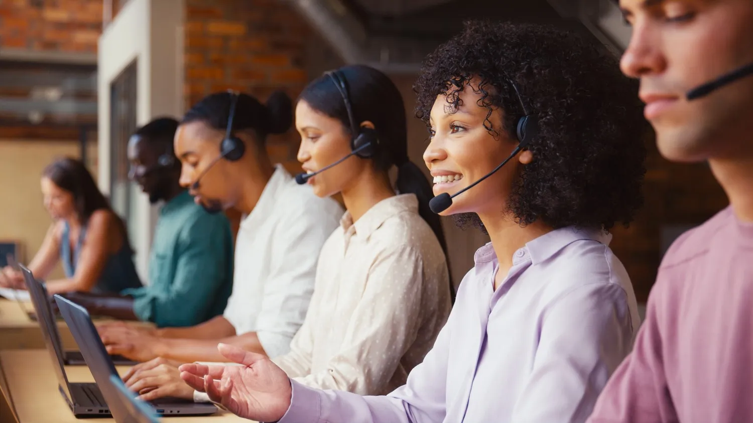 Diverse group of customer service agents wearing headsets working on laptops in a call center.