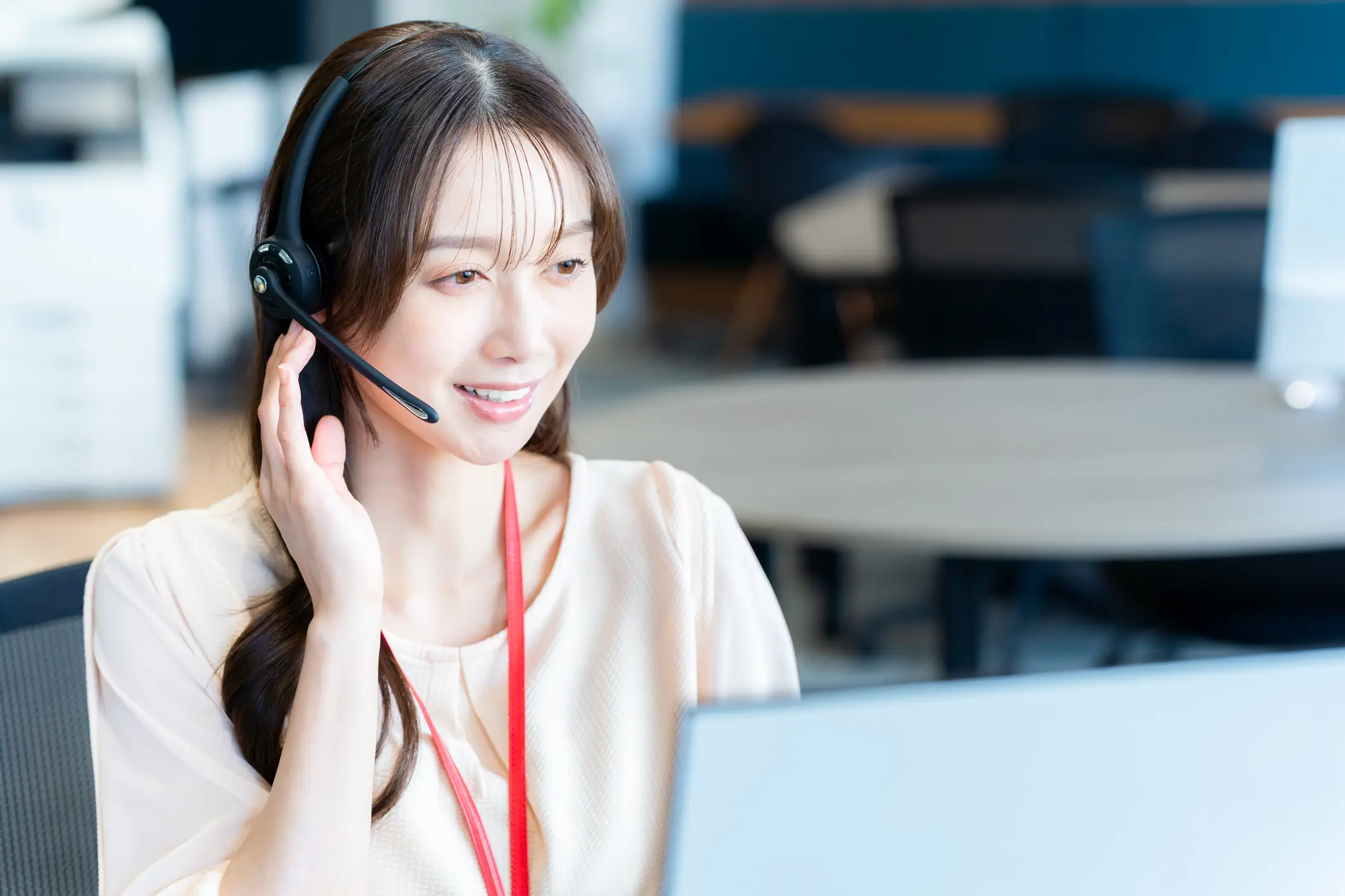 Friendly Asian customer service agent with a headset and red lanyard looking at a computer.
