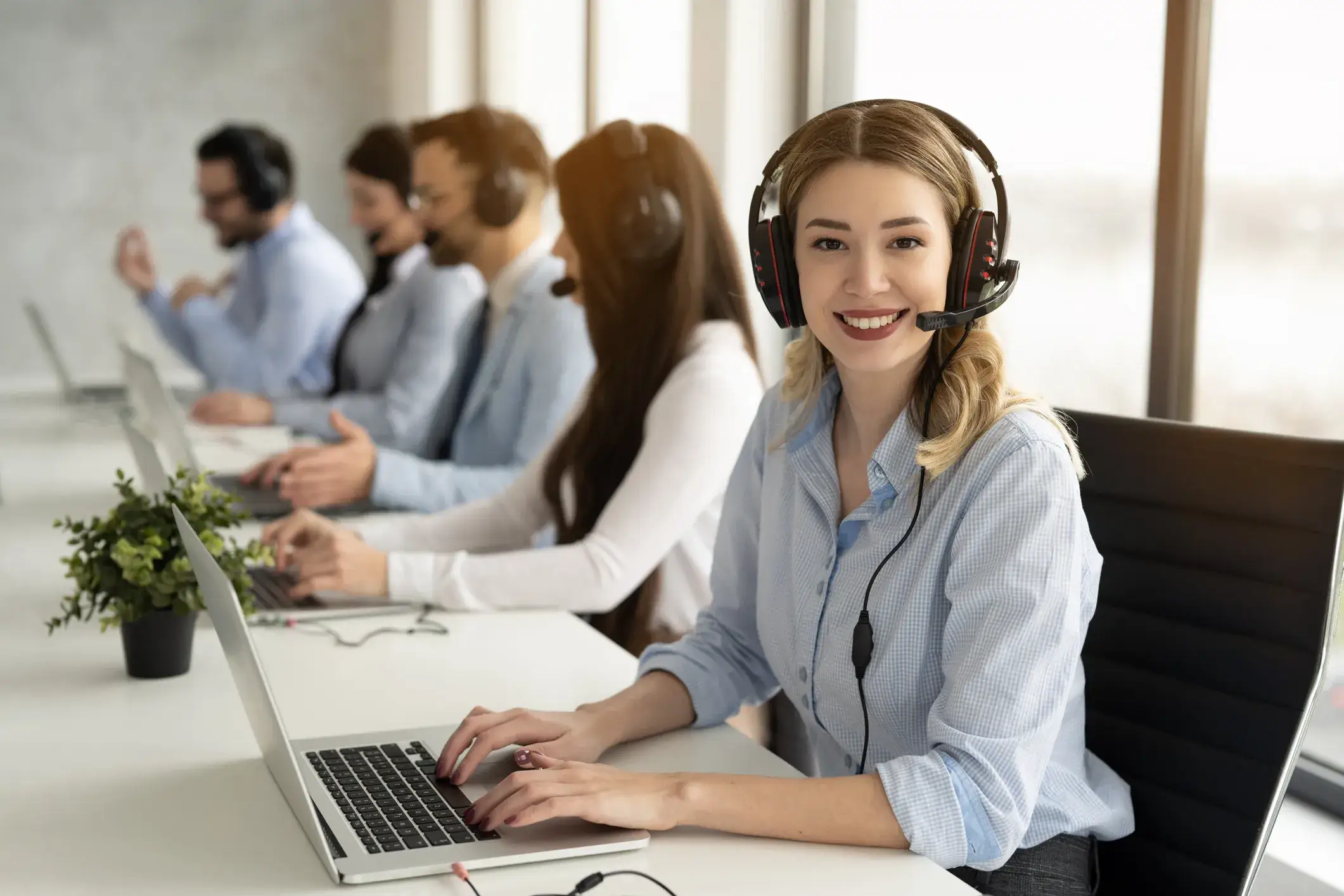 Smiling female agent wearing a headset and working at a modern call center.