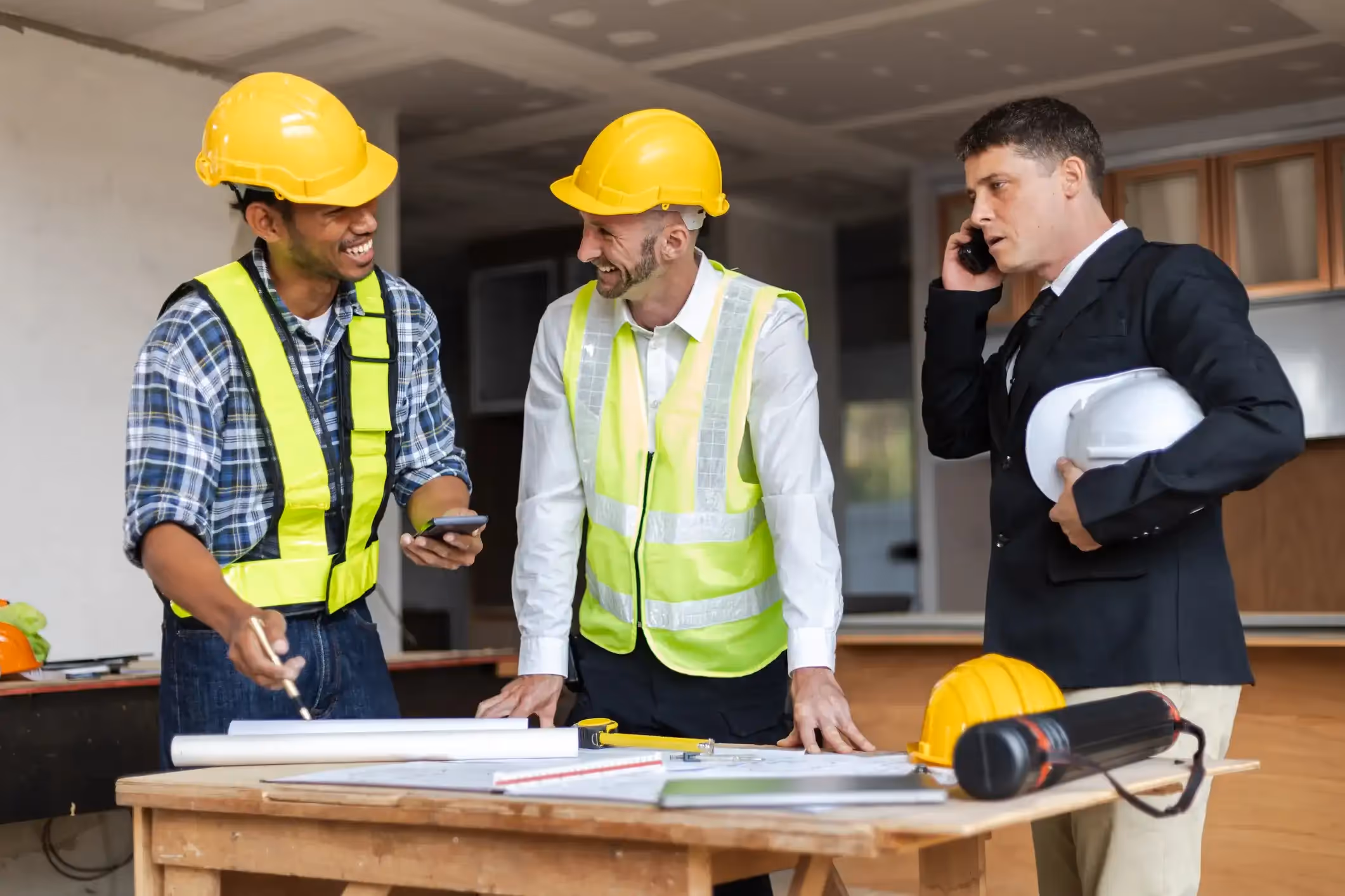 Three construction professionals reviewing plans and talking on a job site.