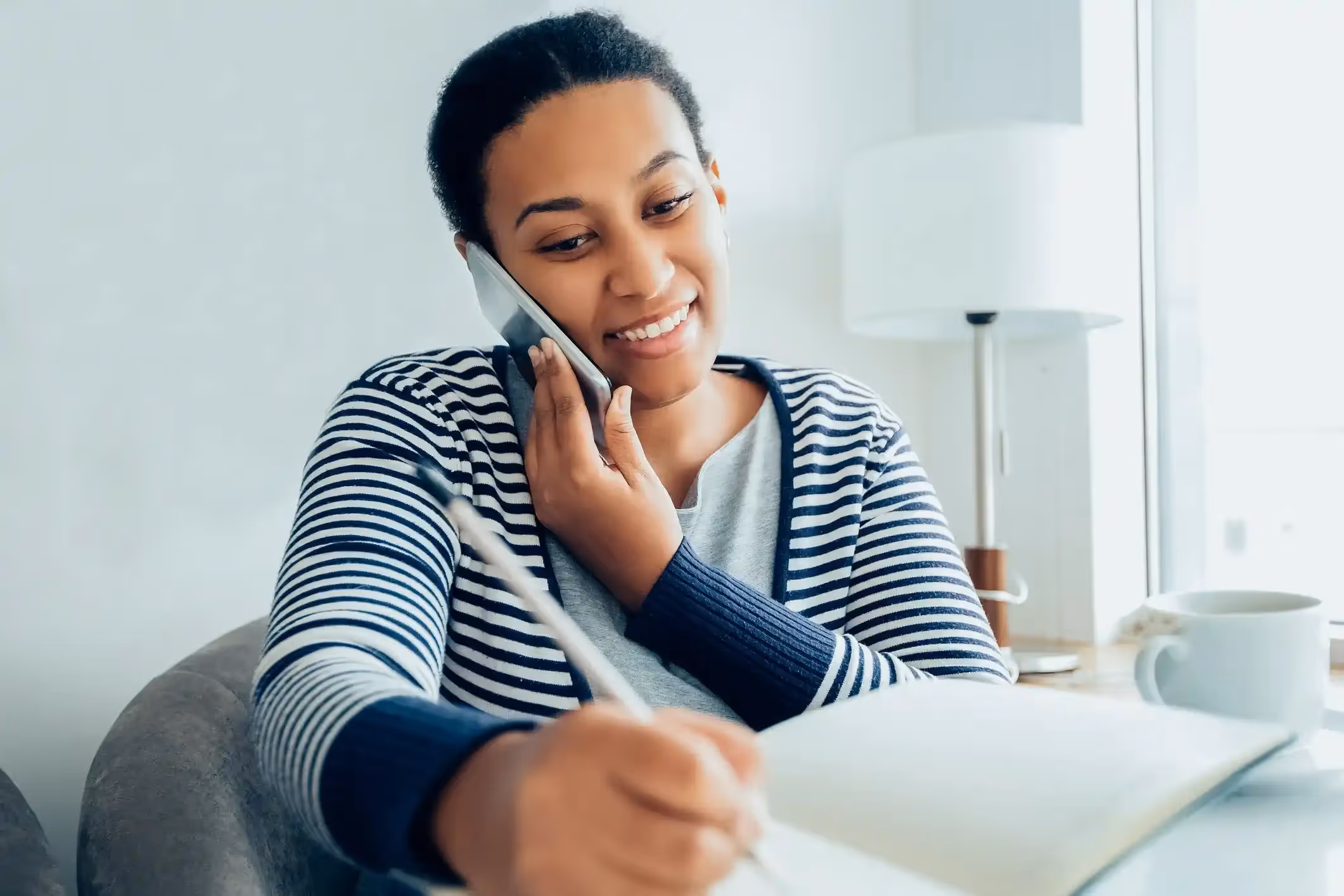 Smiling woman on a mobile phone taking notes in a planner.