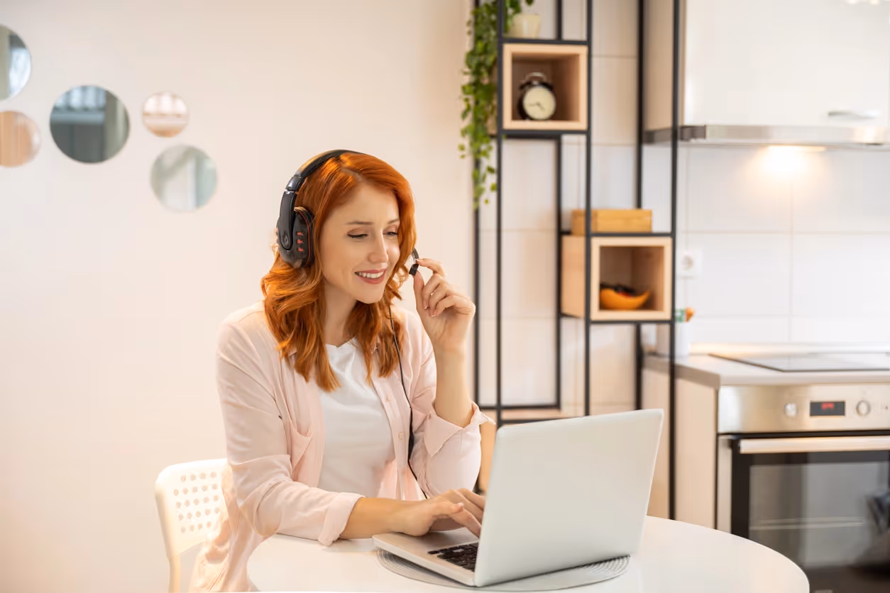 A woman with red hair smiles while wearing headphones and talking into a microphone. 