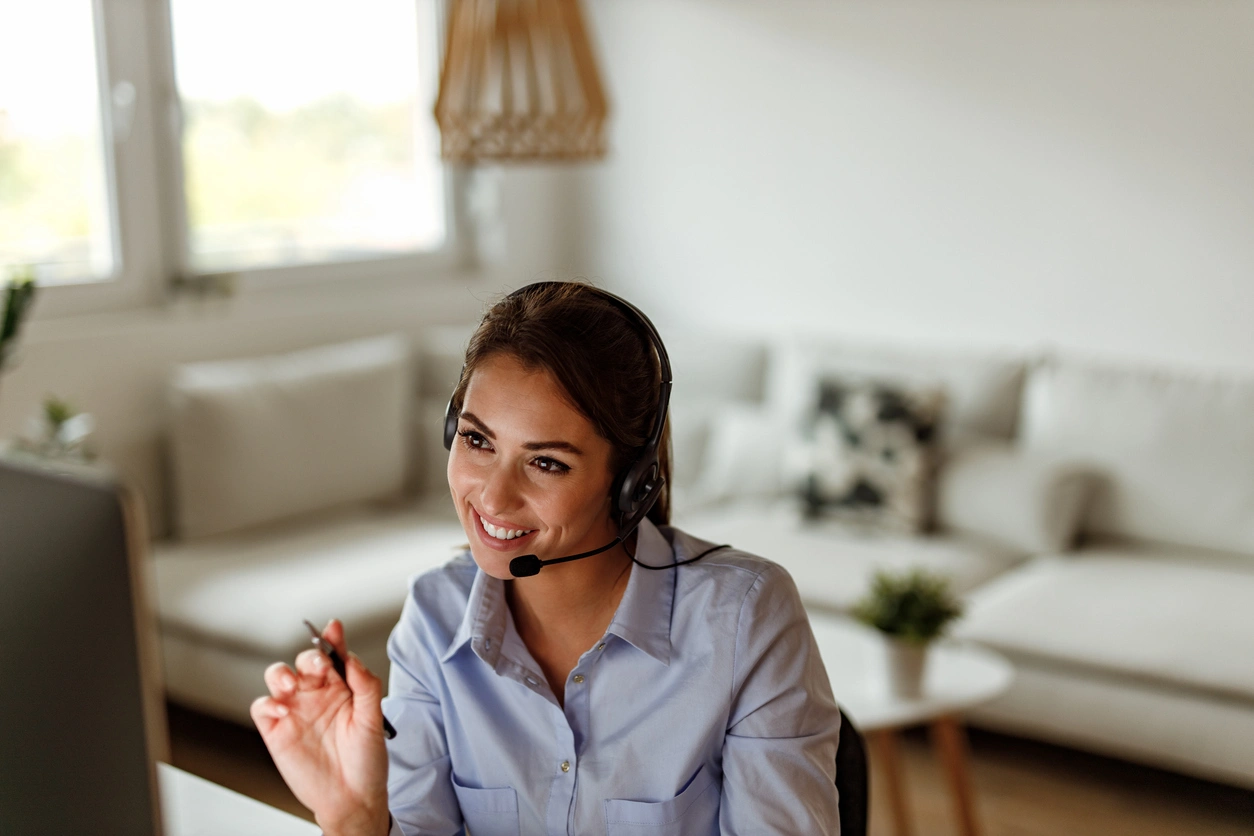 Smiling woman in a light blue shirt wearing a headset, engaging in a video call. 