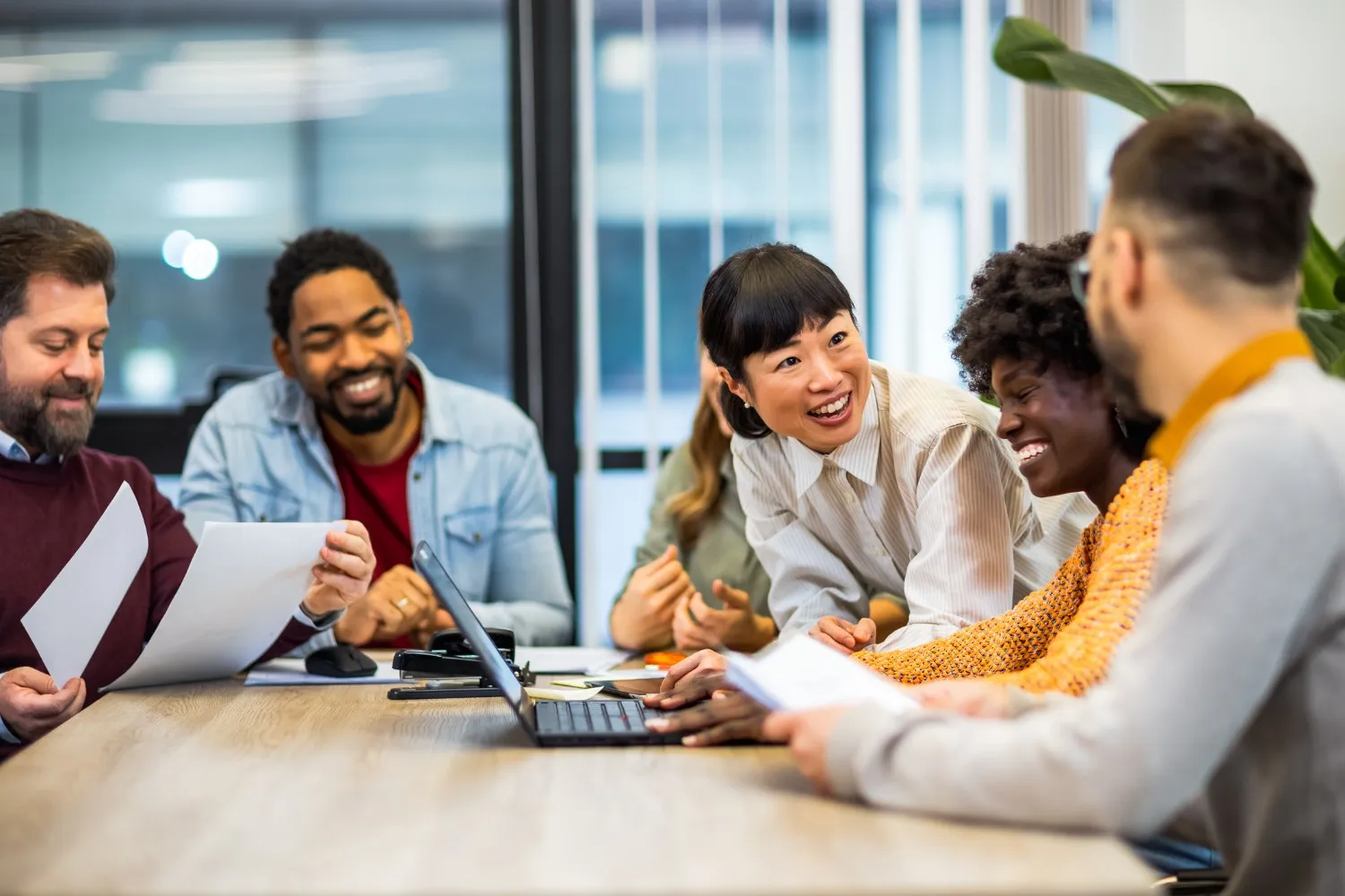 A diverse group of smiling professionals collaborating around a conference table with a laptop and documents.