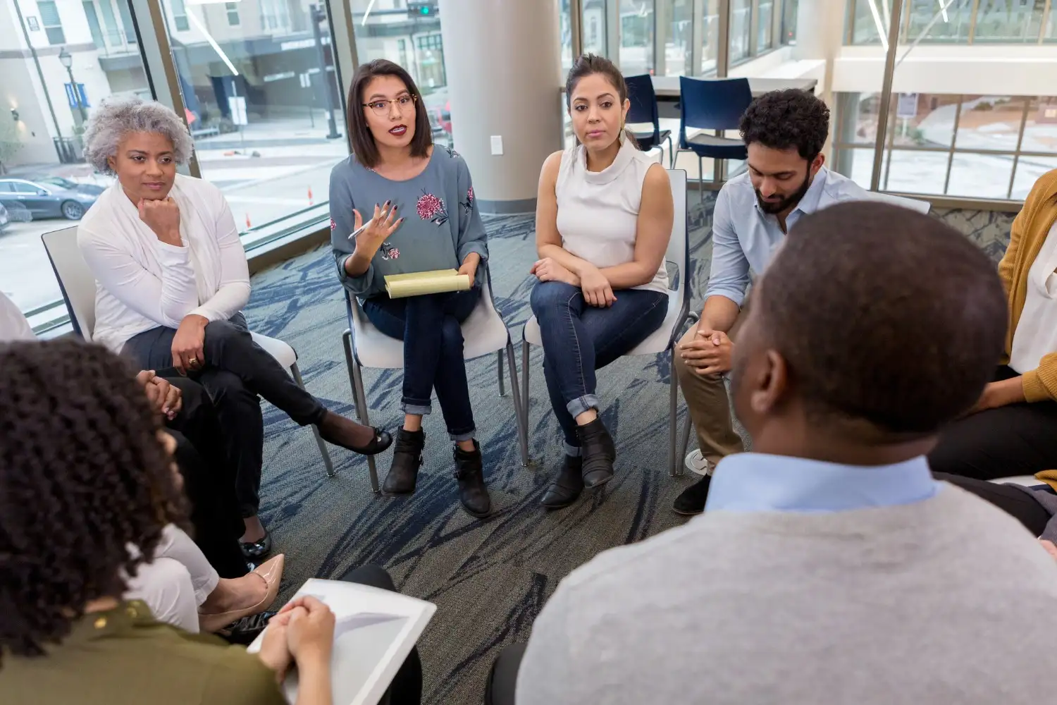 A diverse group of people sitting in a circle of chairs, engaged in a focused group discussion.