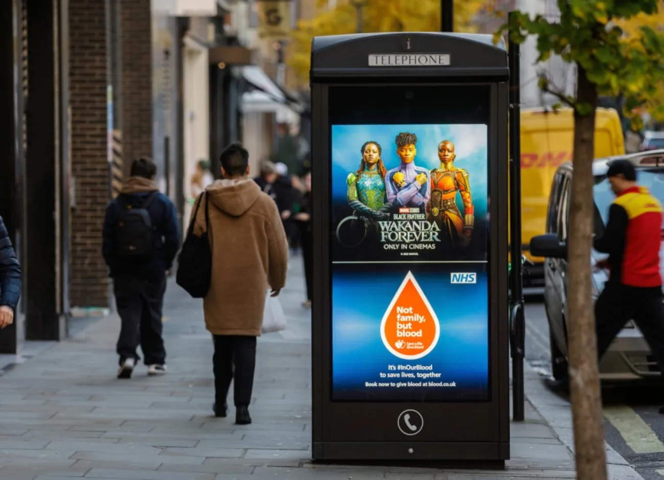 A digital payphone screen with a NHS ad campaign
