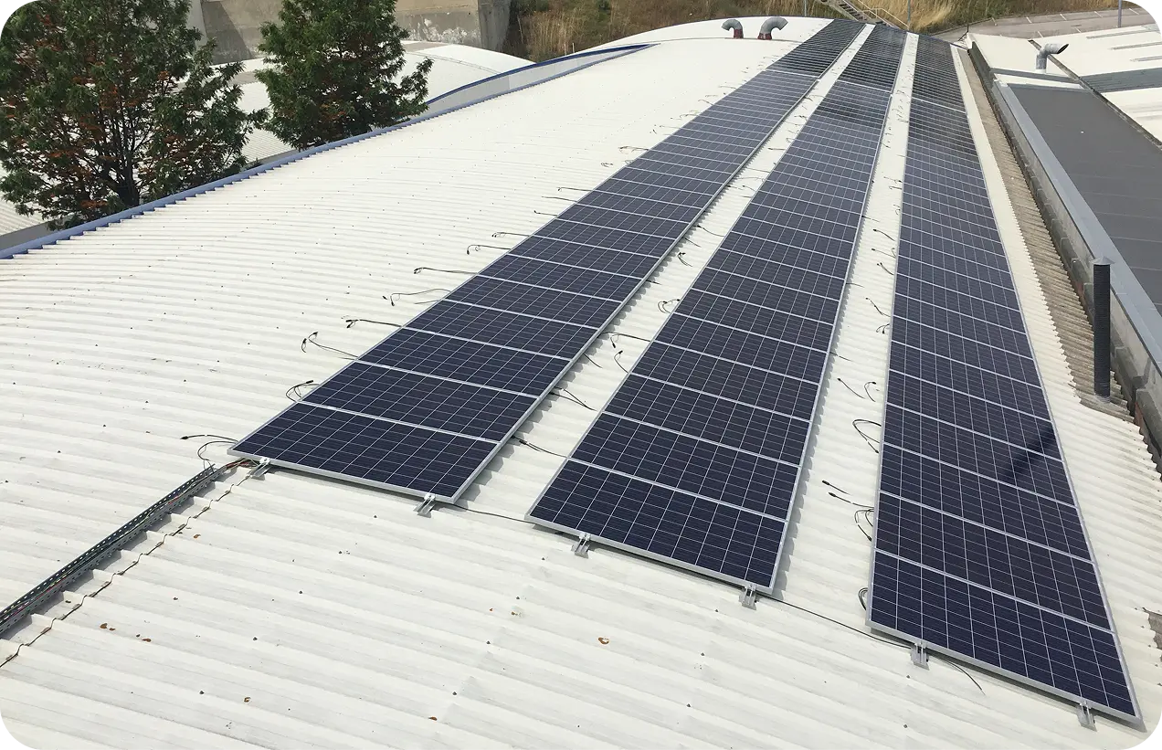 Rural building with solar panels on roof, various equipment outside, under a partly cloudy sky.