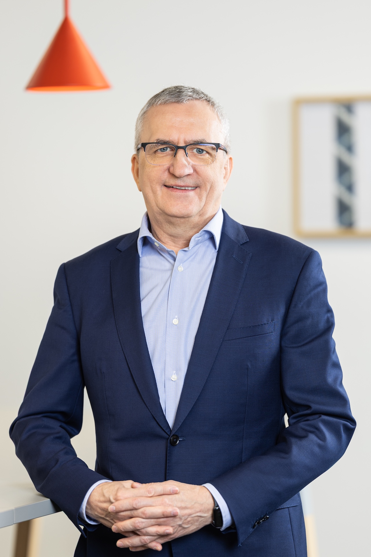 Uśmiechnięty mężczyzna w jasnej koszulce i ciemnej marynarce na jasnym tle.