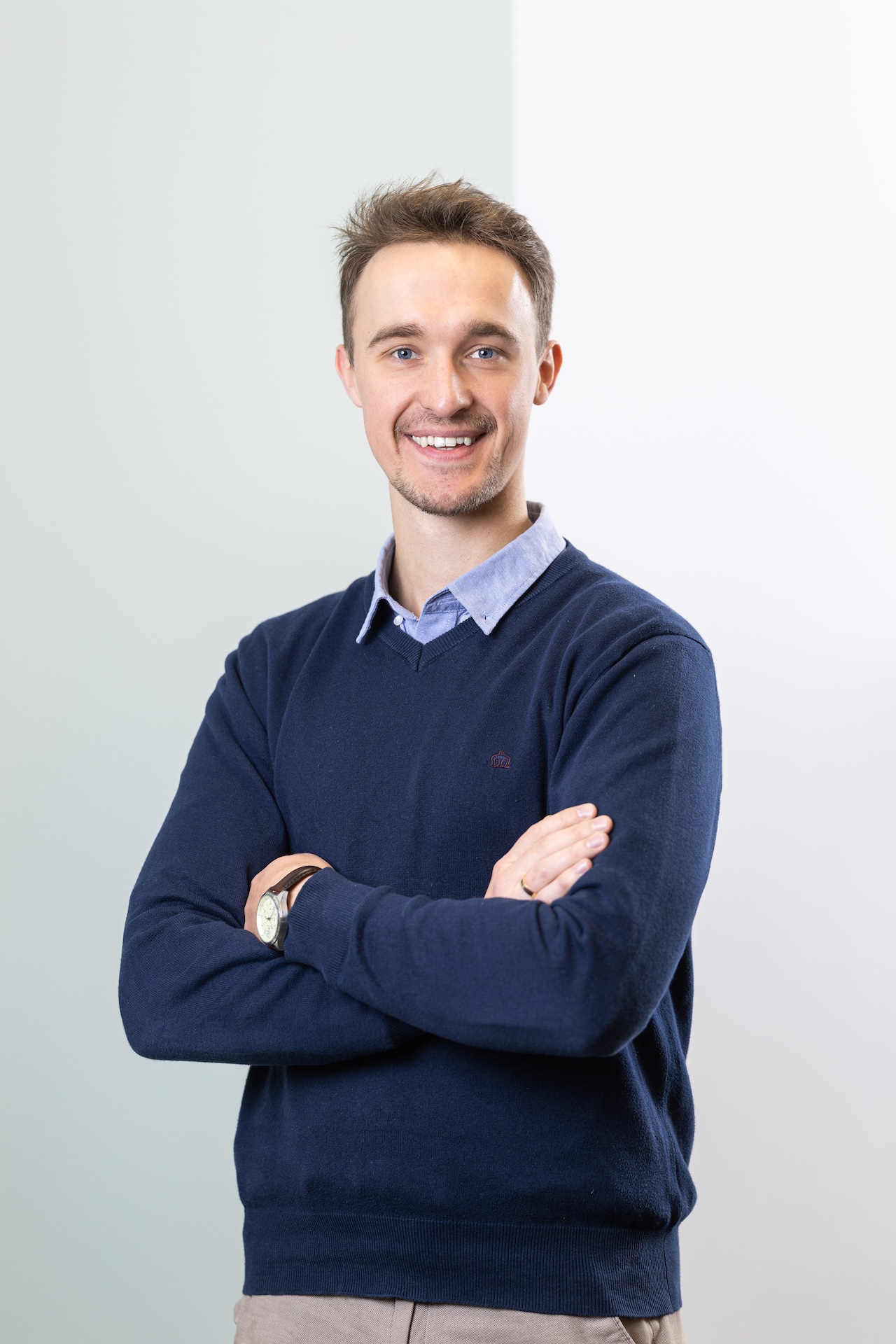 Kobieta o ciemnych włosach, nosząca okulary i szary golf, patrzy prosto przed siebie na jasnoszarym tle.