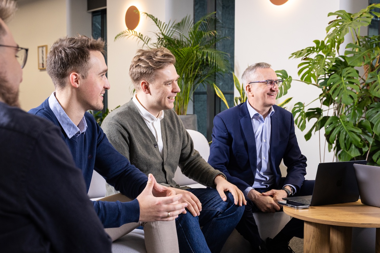 Kobieta o ciemnych włosach, nosząca okulary i szary golf, patrzy prosto przed siebie na jasnoszarym tle.