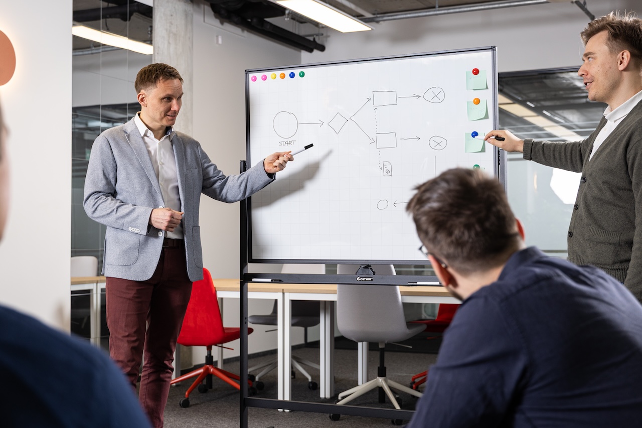 Uśmiechnięty mężczyzna w jasnej koszulce i ciemnej marynarce na jasnym tle.