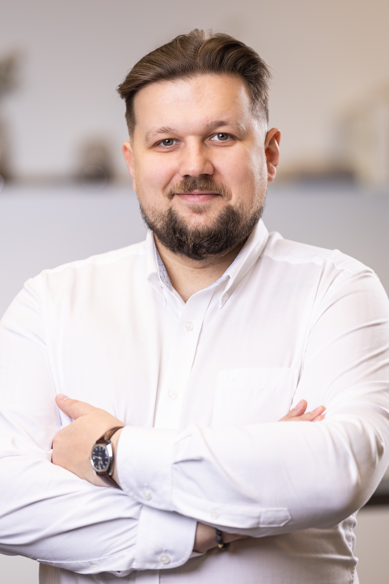 Uśmiechnięty mężczyzna w jasnej koszulce i ciemnej marynarce na jasnym tle.