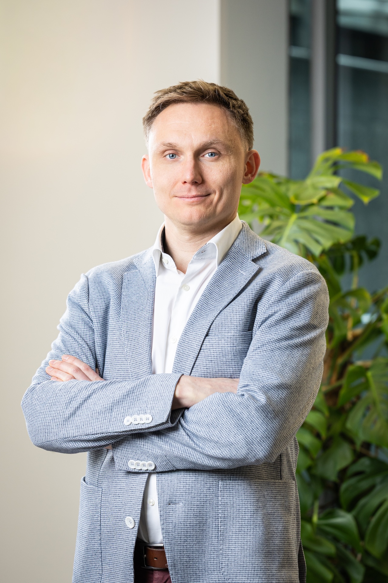 Uśmiechnięty mężczyzna w jasnej koszulce i ciemnej marynarce na jasnym tle.