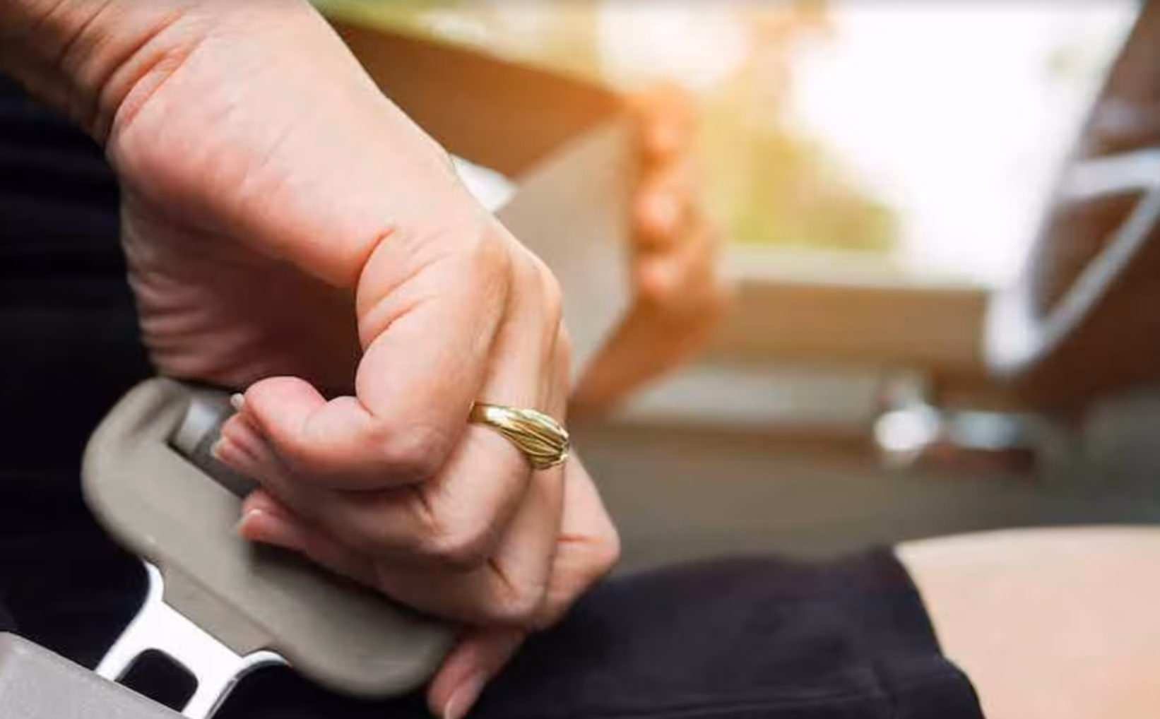 Hand met gouden ring die een autogordel vastmaakt.