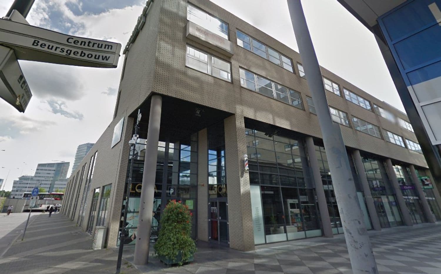 Modern kantoorgebouw met grote ramen en pijlers aan een stadsstraat in Eindhoven, met een straatnaambord 'Centrum Beursgebouw'.