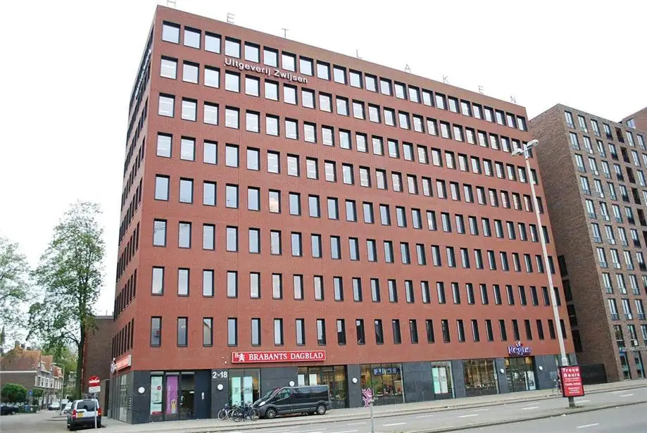 Groot hoekgebouw met rode bakstenen en veel ramen, met borden van Uitgeverij Zwijsen en Brabants Dagblad.