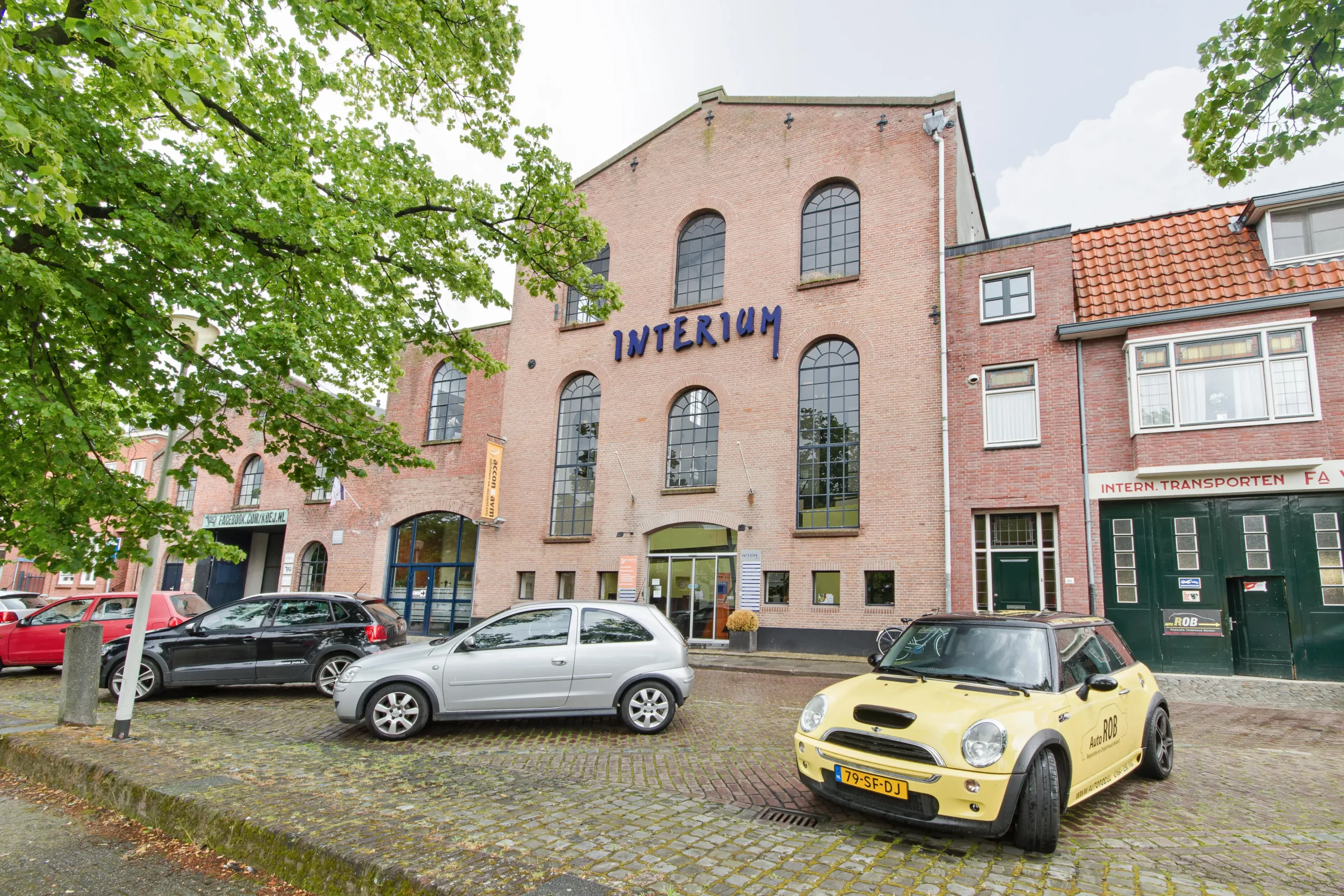 Gevel van een bakstenen gebouw met de naam Interim en geparkeerde auto's op een kasseienplein.