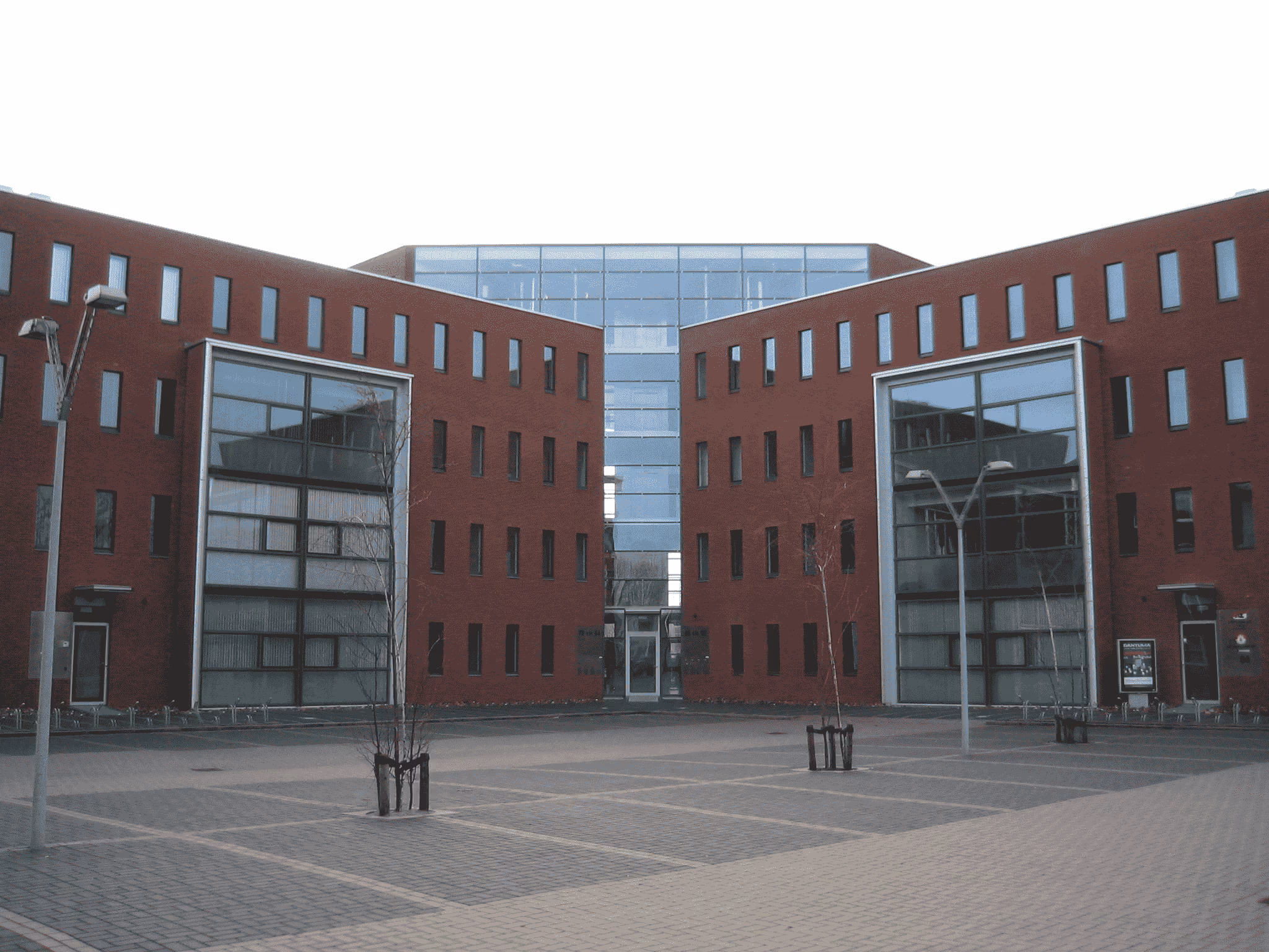 Moderne kantoorgebouwen met rode bakstenen en grote glasramen rondom een open plein met bestrating en straatlantaarns.