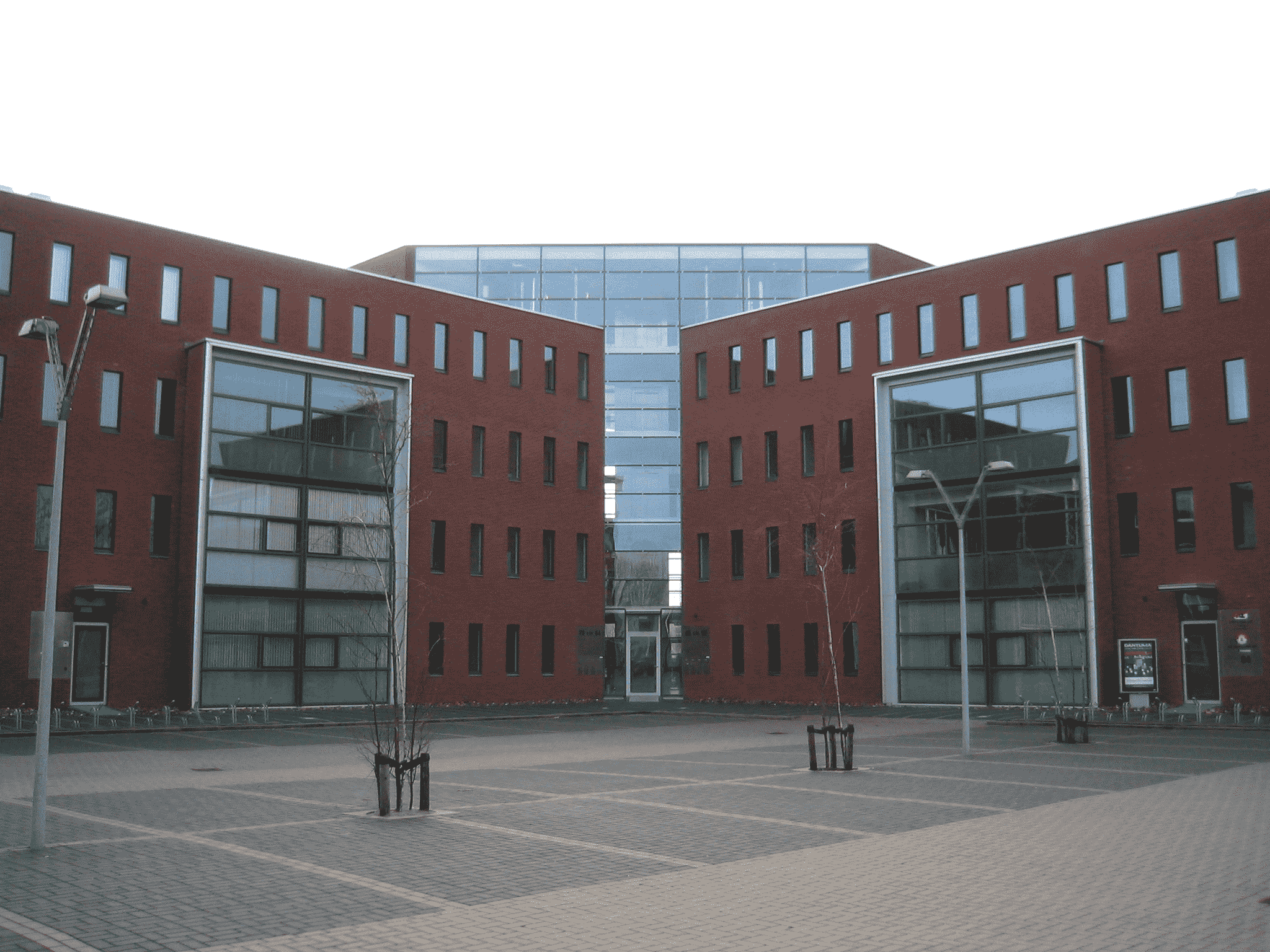 Moderne kantoorgebouwen met rode bakstenen en grote glasramen rondom een open plein met bestrating en straatlantaarns.