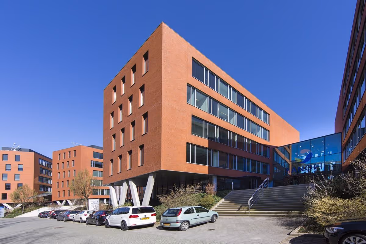 Moderne kantoorgebouwen met koperkleurige gevels en grote ramen onder een heldere blauwe lucht, geparkeerde auto's op de voorgrond.