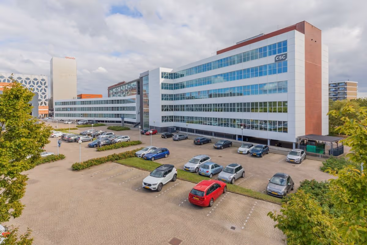 Parkeerterrein met auto's voor een modern kantoorgebouw met het CSC-logo op de gevel.
