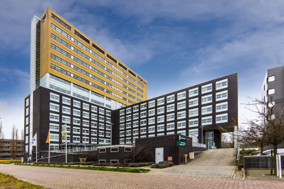 Modern kantoorgebouw met zwart en geel gevel en grote ramen onder een bewolkte blauwe hemel.
