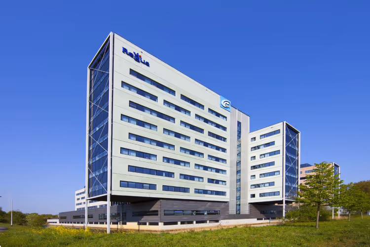 Modern kantoorgebouw met glazen wanden en het logo van Radboud op een zonnige dag met blauwe lucht.