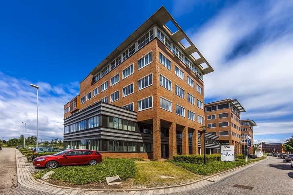 Moderne kantoorgebouwen met rode bakstenen en grote ramen onder een partly bewolkte blauwe lucht.