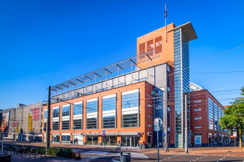 Moderne oranje en glazen kantoorgebouw aan een stadsweg onder een heldere blauwe lucht.