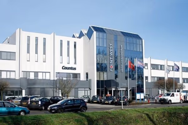 Modern kantoorgebouw met wit exterieur en glazen façade in Almelo, parkeerplaats met auto's ervoor.