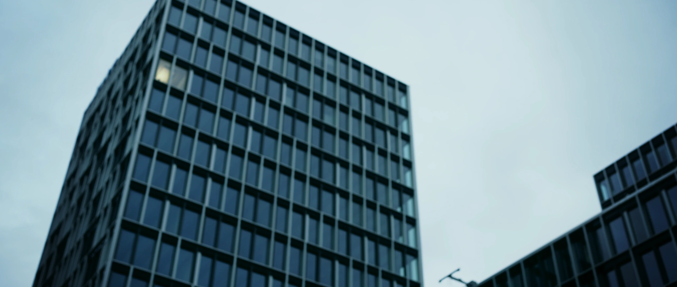 Contre-plongée sur un immeuble de bureaux aux façades de verre sombre, sous un ciel pâle.