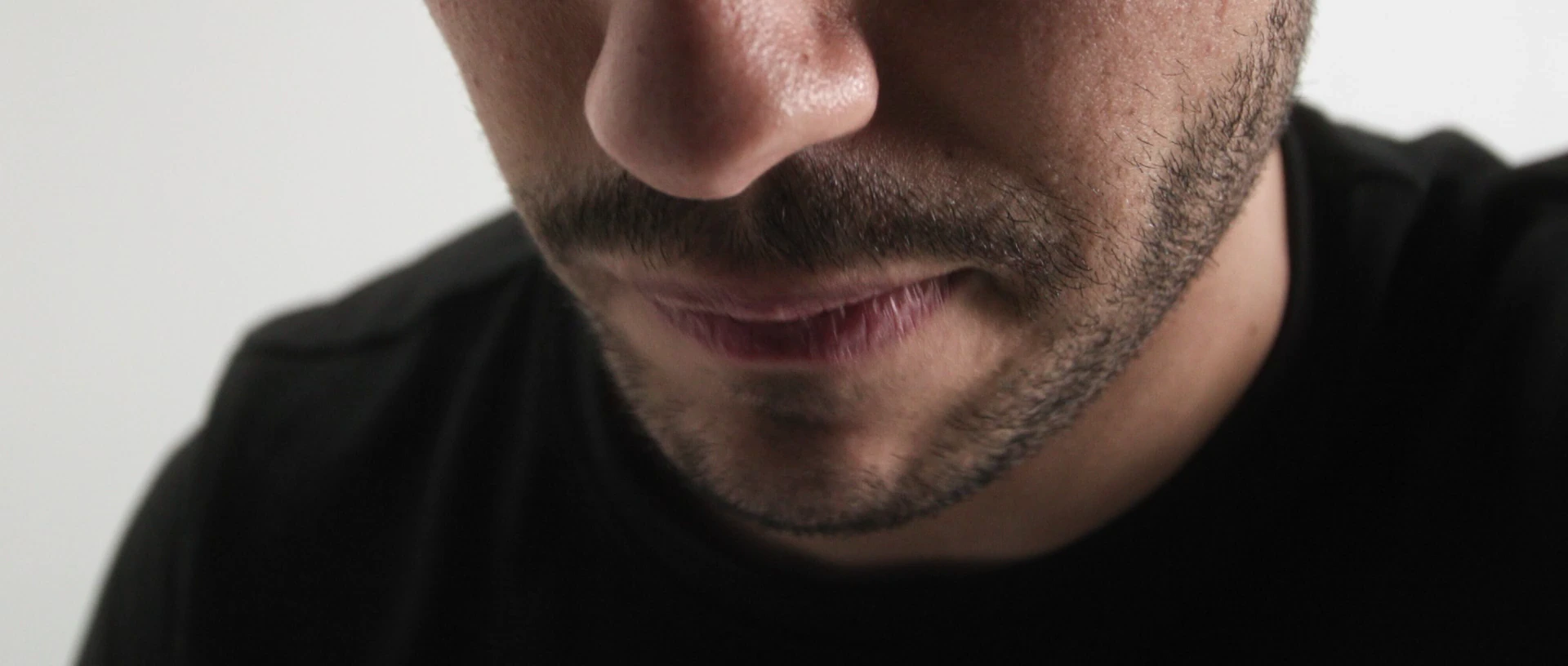 Gros plan sur le bas du visage d'un homme barbu en t-shirt noir, la bouche entrouverte.