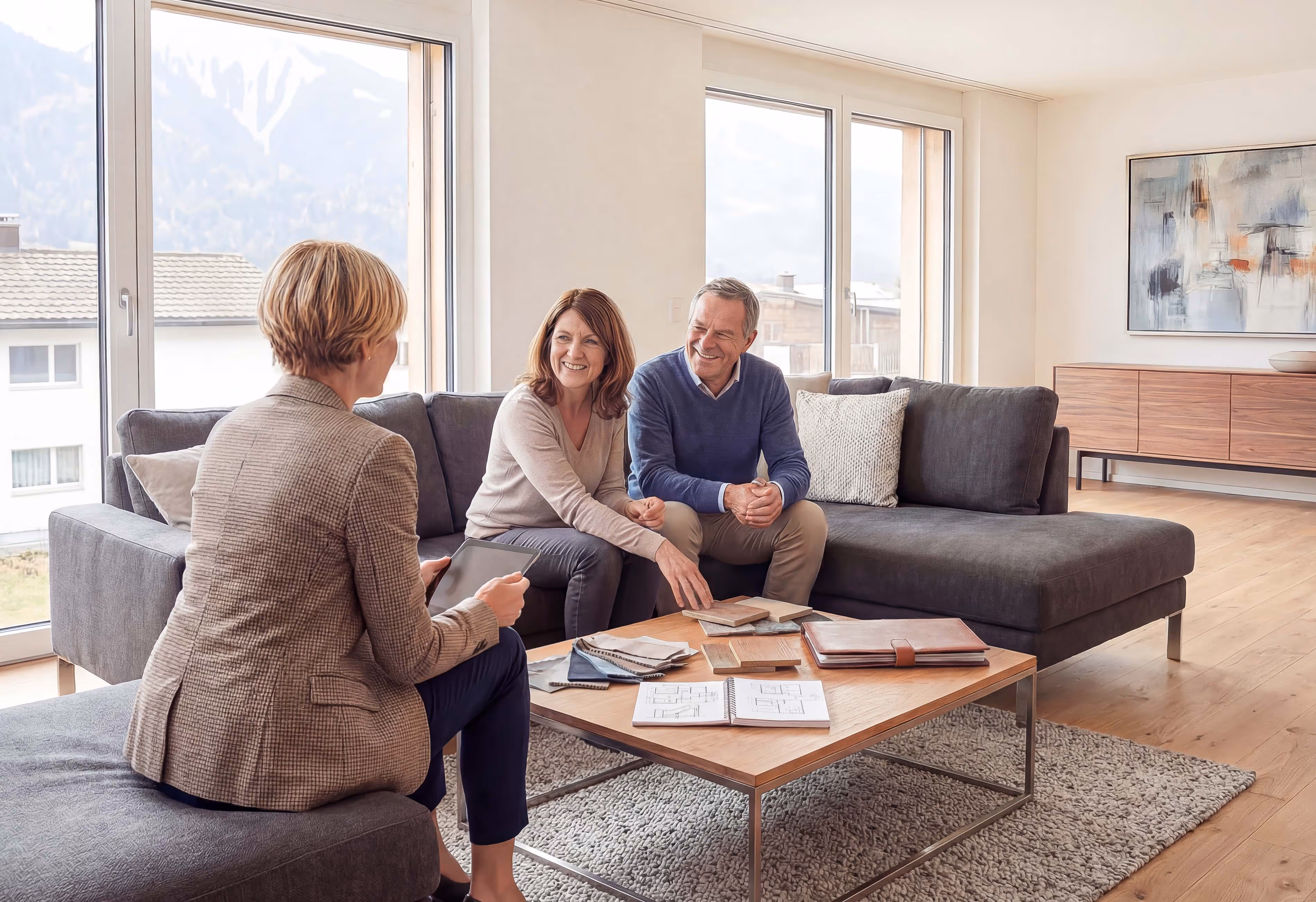 Drei Personen sitzen in einem modernen Wohnzimmer und besprechen Holzproben und Architektenpläne auf einem Couchtisch.