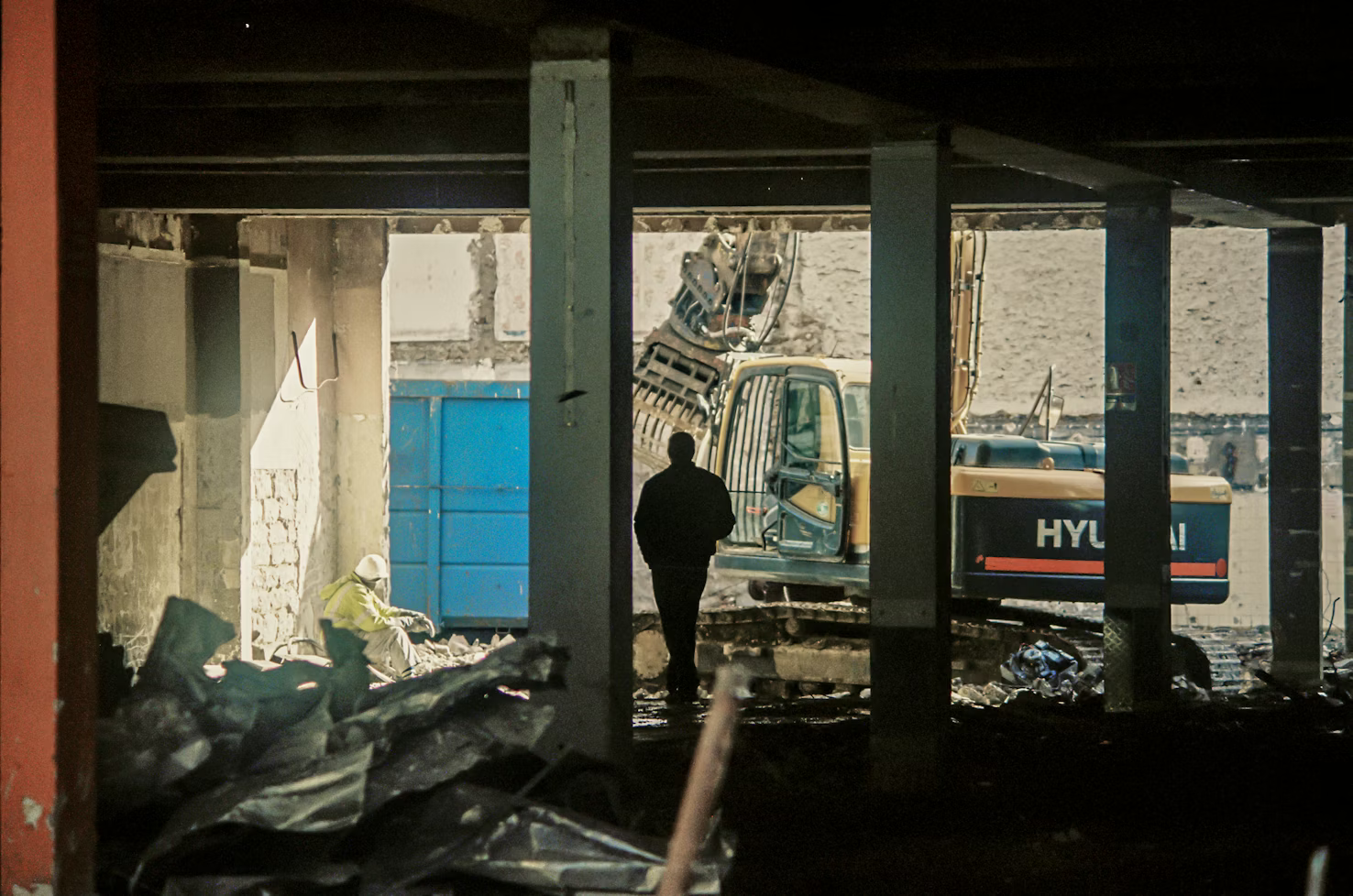 Ouvriers marchant dans l'ombre d'un bâtiment en chantier regardant vers un tractopelle