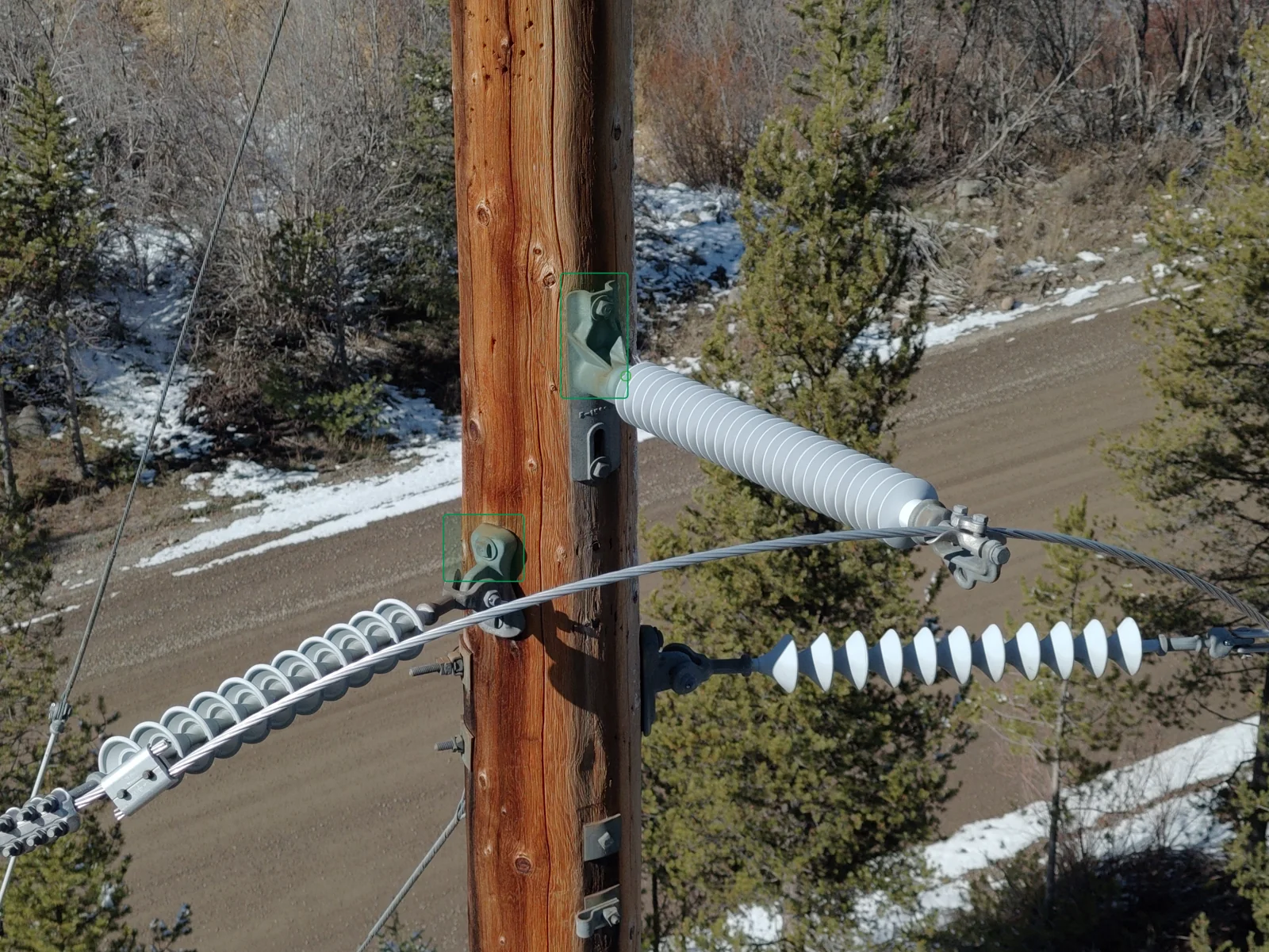 Close-range drone image of pole-top insulator strings, clevis hardware, and conductor attachments on a wooden transmission structure