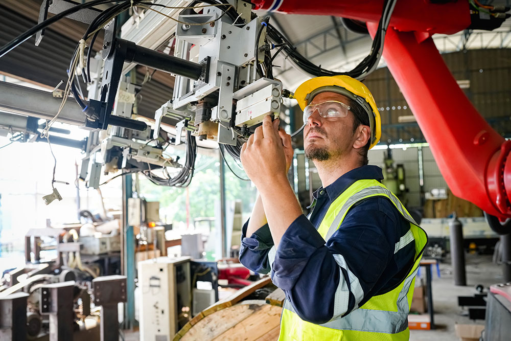 Engineer in a yellow safety helmet and vest inspecting machinery in an industrial workshop.